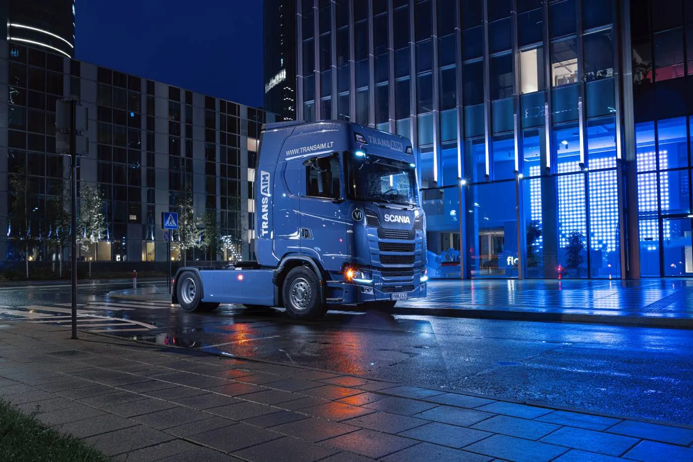 A blue truck in the city street at night time.